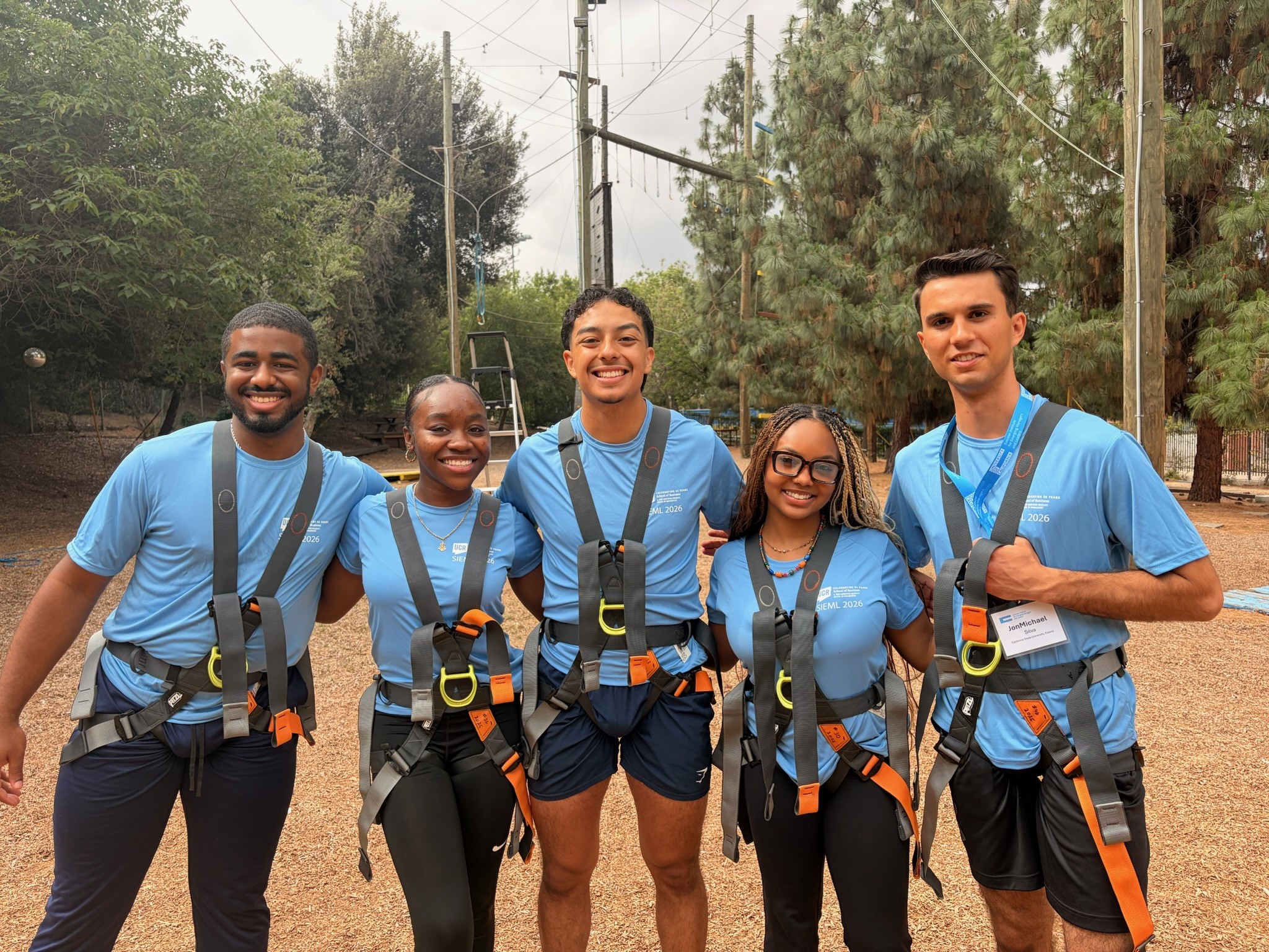 students gathering today, smiling at the camera while wearing harrness before going on a ropes course